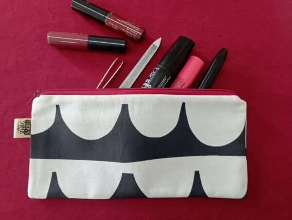 Ein Stoffbeutel mit schwarz-weißem Muster, gefüllt mit verschiedenen Kosmetikartikeln, darunter Lippenstifte und eine Nagelfeile.